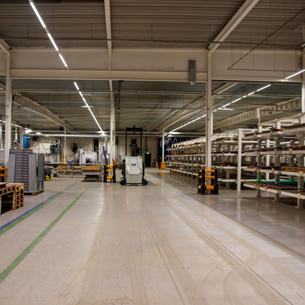 A clean factory floor: a pick-and-place machine on the left, racks of parts on the right