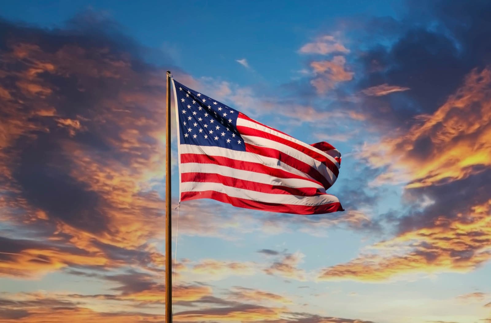 An American flag on a pole, flying whole against a sunset sky